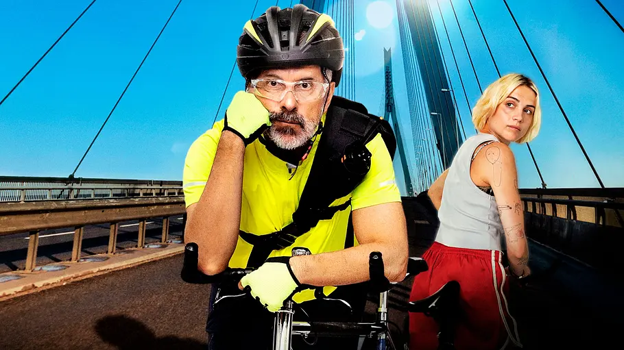 Bert (Christoph Maria Herbst) lehnt in neongelber Radkleidung auf einem Fahrrad. Les (Mala Emde) steht neben ihm auf einer Brücke.