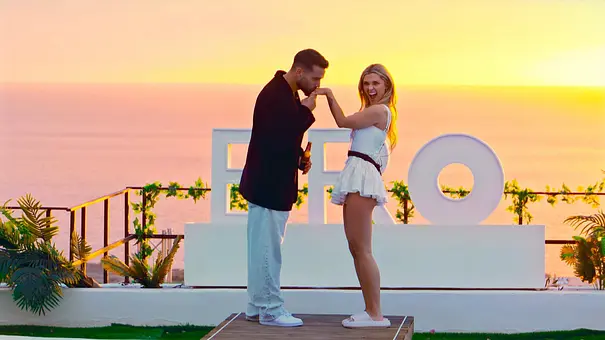 Josh küsst Nasrin bei Sonnenuntergang die Hand. Das Paar steht vor einem „BRO“-Schriftzug mit Blick auf das Meer - Foto: RTL Josh küsst Nasrin bei Sonnenuntergang die Hand. Das Paar steht vor einem „BRO“-Schriftzug mit Blick auf das Meer - Foto: RTL