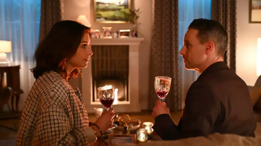 Gabriella und Kilian sitzen vor einem Kamin und trinken Wein.