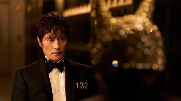 Der Frontmann sitzt mit resignierten Blick vor einer Person mit Hasenmaske. - Foto: No Ju-han/Netflix Der Frontmann sitzt mit resignierten Blick vor einer Person mit Hasenmaske. - Foto: No Ju-han/Netflix