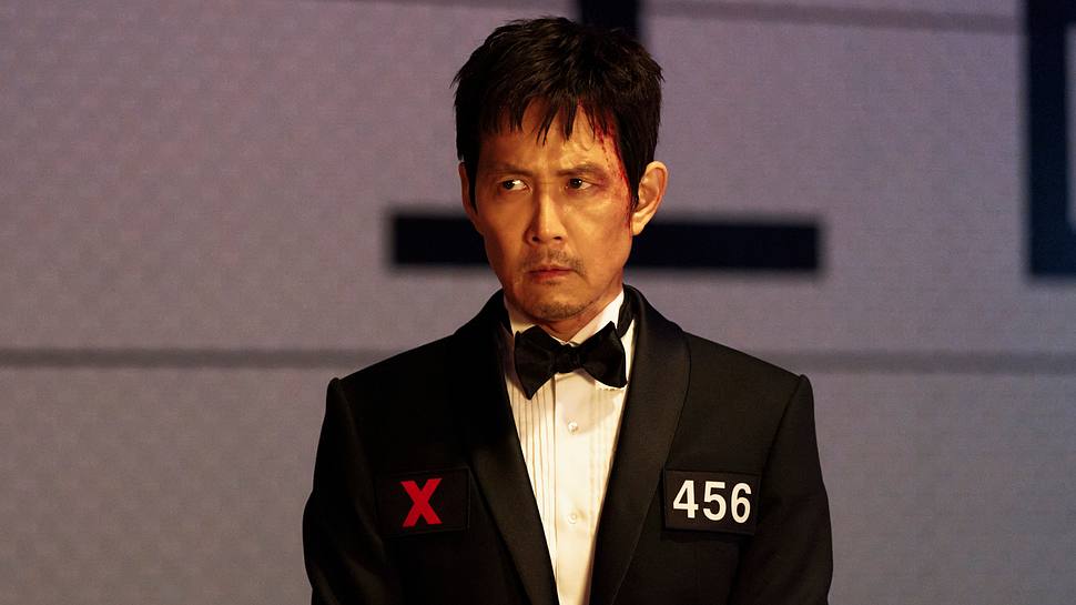 Gi-Hun sitzt einem schwarzem Smoking mit einem blutigen Gesicht - Foto: No Ju-han/Netflix