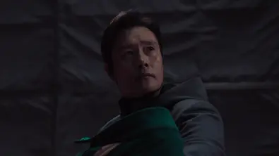 Lee Byun-hun hält in seiner Rolle als Frontmann ein Baby (Spielerin 222) im Arm und blickt in die Ferne - Foto: Netflix