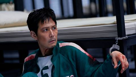 Gi-hun ist mit Handschellen an sein Bett gekettet und schaut mit einem traurigem Bilck in die Ferne. - Foto: No Ju-han/Netflix