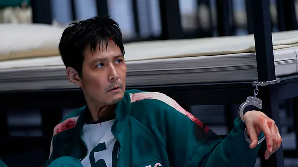 Gi-hun ist mit Handschellen an sein Bett gekettet und schaut mit einem traurigem Bilck in die Ferne. - Foto: No Ju-han/Netflix Gi-hun ist mit Handschellen an sein Bett gekettet und schaut mit einem traurigem Bilck in die Ferne. - Foto: No Ju-han/Netflix