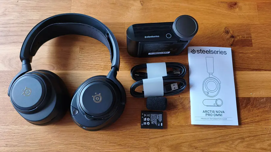 Das Steelseries Arctis Nova Pro Omni mit Zubehör liegt auf einem Holztisch