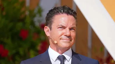 Stefan Mross beim Ende von Immer wieder sonntags. Er trägt einen dunkelblauen Anzug mit Krawatte und trägt ein Headset-Mikrofon. - Foto: IMAGO / HOFER Stefan Mross beim Ende von Immer wieder sonntags. Er trägt einen dunkelblauen Anzug mit Krawatte und trägt ein Headset-Mikrofon. - Foto: IMAGO / HOFER