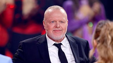 Stefan Raab sitzt im Anzug und lächelt leicht - Foto: IMAGO / Panama Pictures