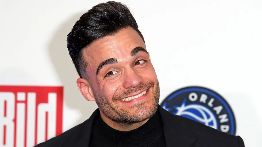 Stefano Zarrella Stefano Zarella steht mit einem breiten Grinsen vor einer Pressewand. Er ist schwarz gekleidet.
