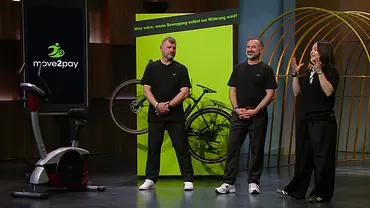 Steffen Baumgart, Karim und Mia Allouche stehen neben einem Heimtrainer und einem Fahrrad vor einer grünen „move2pay“-Kulisse. - Foto: RTL Steffen Baumgart, Karim und Mia Allouche stehen neben einem Heimtrainer und einem Fahrrad vor einer grünen „move2pay“-Kulisse. - Foto: RTL