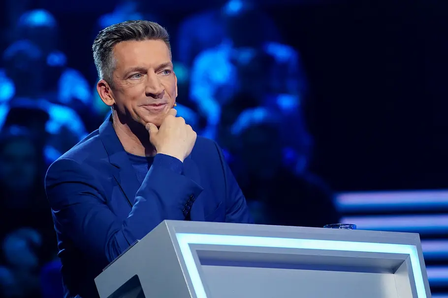 Steffen Hallaschka sitzt am Pult seiner neuen Quizshow und stützt sein Kinn auf seine Hand.