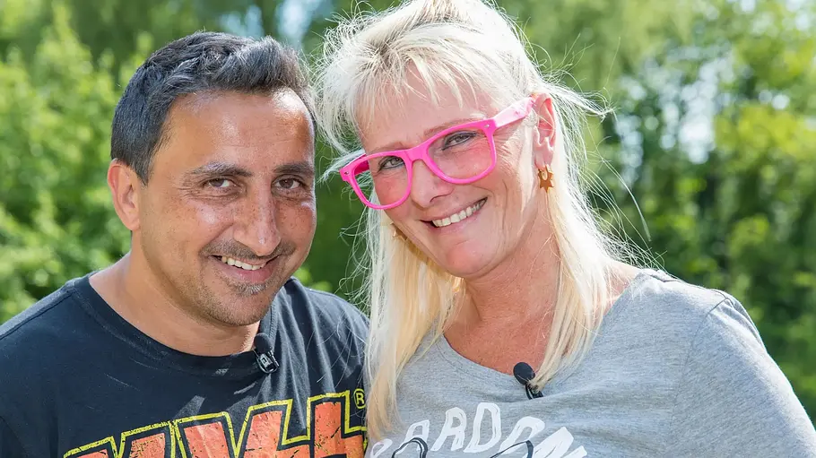 Steffi und Roland Bartsch Roland und Steffi Bartsch lächeln vor grünen Bäumen in die Kamera. Er trägt ein KISS-Shirt, sie eine pinke Brille.