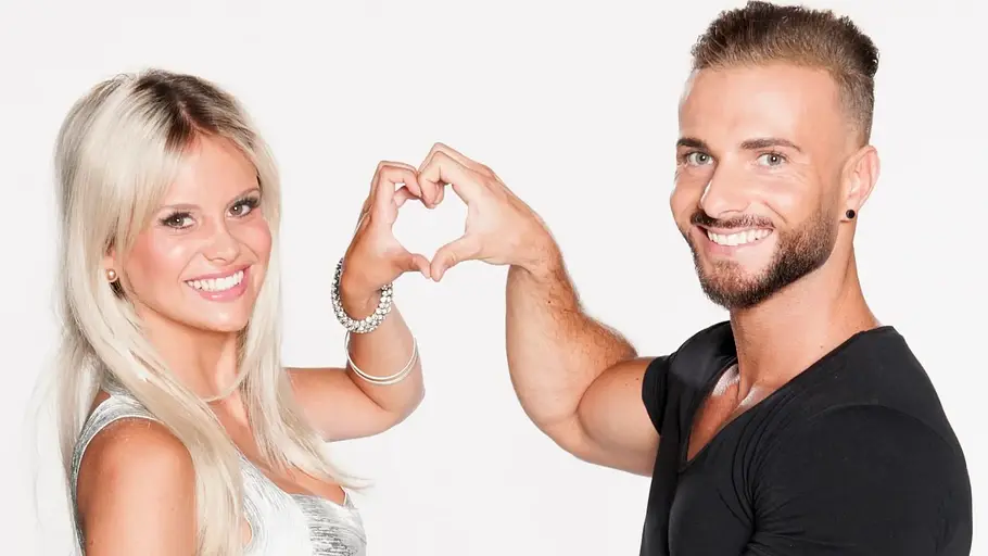 Stephanie Schmitz und Julian Evangelos Stephanie Schmitz und Julian Evangelos lächeln in die Kamera und formen gemeinsam mit ihren Händen ein Herz.