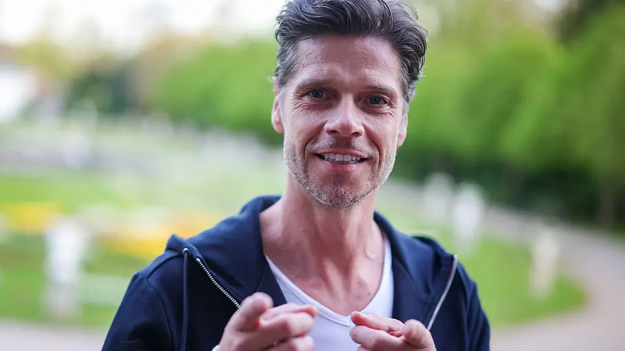 Stephen Dürr wagt den Schritt zu Promis unter Palmen. Stephen Dürr zeigt mit seinen Fingern zur Kamera.