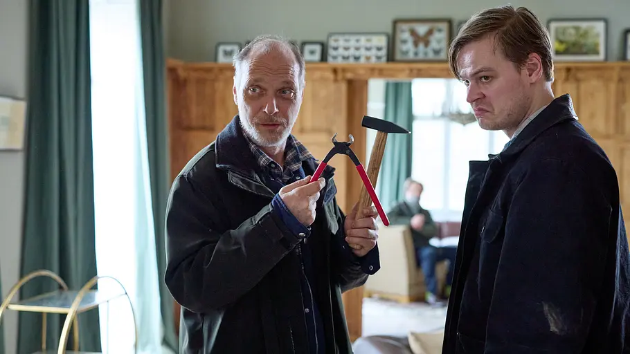 Detlev Schulte (Martin Brambach) und sein Sohn Hannes (Marius Ahrendt) stehen im Durchgang eines Wohnzimmers. Im Hintergrund sitzt, unscharf zu erkennen, eine geknebelte Person, Peter Unger (Steffen Münster), auf einem Sessel. Detlev hält mit maliziösem Lächeln eine Zange und einen Hammer in die Höhe, Hannes steht daneben und blickt grimmig.