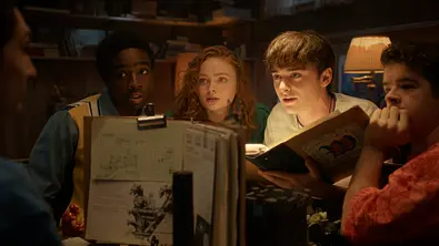 Fünf Jugendliche sitzen an einem Tisch zusammen. Vier von ihnen schauen einen gespannt und fragend an. - Foto: Netflix © 2025