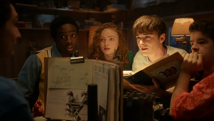 „Stranger Things“-Spin-off Fünf Jugendliche sitzen an einem Tisch zusammen. Vier von ihnen schauen einen gespannt und fragend an.