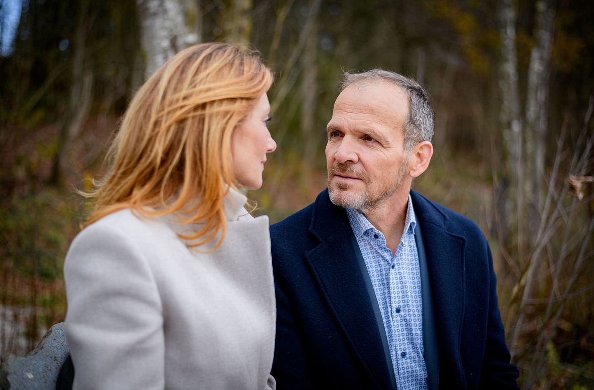 Alexandra und Markus schauen sich innig an, als sie gemeinsam auf einer Parkbank sitzen