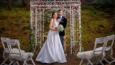 Maxi und Henry sind im Hochzeitskleid bzw. Anzug zu sehen. Sie stehen vor dem Wunschbrunnen und schauen glücklich in die Kamera - Foto: ARD/Christof Arnold