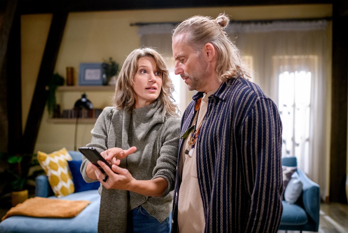 Anja steht zusammen mit Michael im Appartement. Sie zeigt ihm etwas auf ihrem Handy und schaut ihn dabei an!
