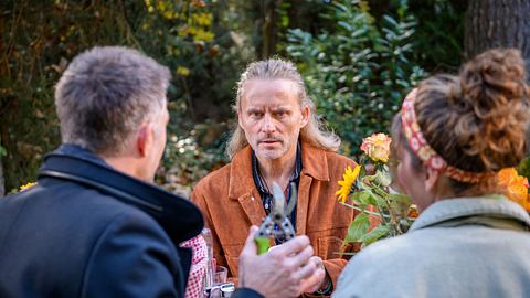 Michael sitzt mit weiteren Figuren an einem Tisch und schaut sehr ernst in die Kamera - Foto: ARD/WDR/Christof Arnold