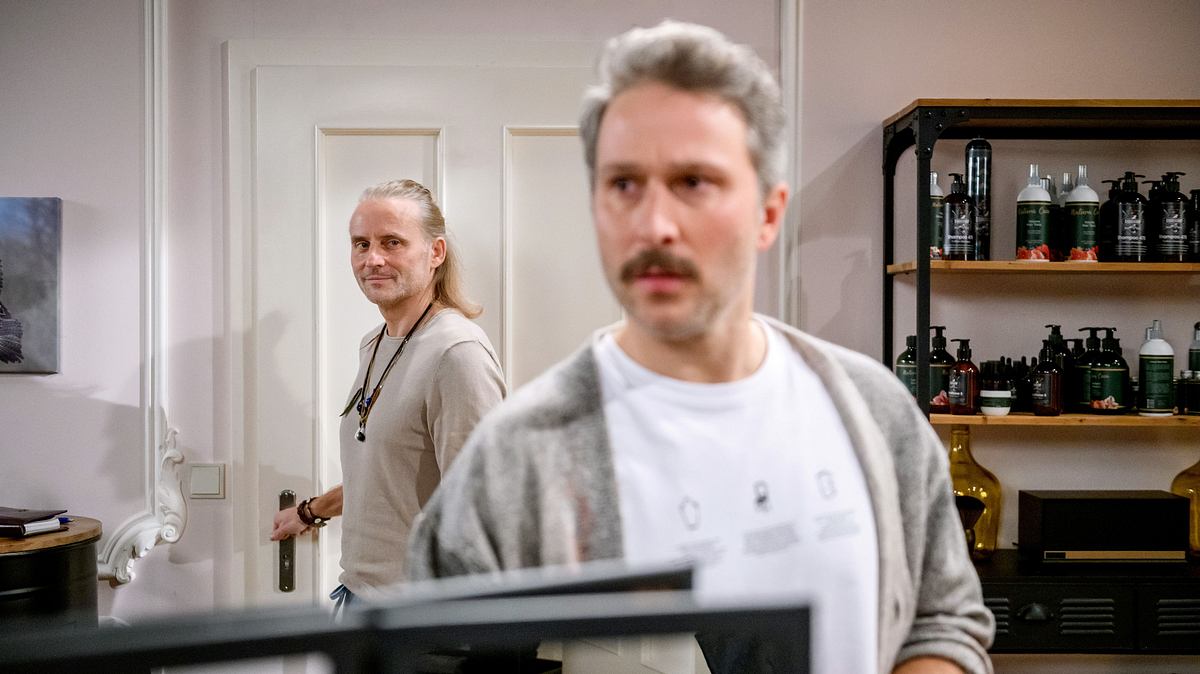 Miro steht verschwommen im Vordergrund und wird von Michael beobachtet, der seine Hand an der Türklinge hat.