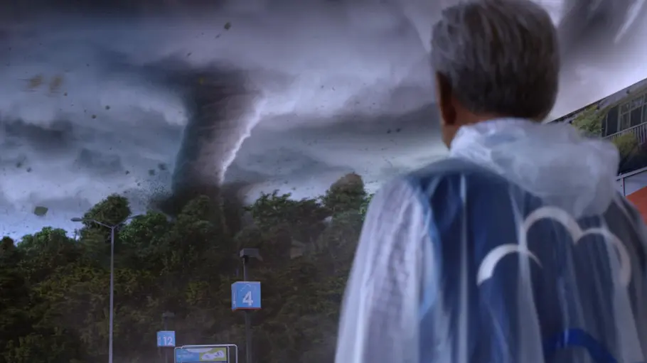 Superstore Ein Mitarbeiter steht im Regenponcho vor einem gewaltigen Tornado, der sich über dem Parkplatz einer Filiale zusammenbraut. Dunkle Gewitterwolken und herumwirbelnde Trümmer sorgen für eine dramatische Szene aus „Superstore“.
