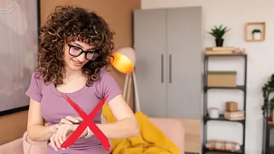 Eine Frau mit Locken und Brille schaut auf ihre Smartwatch. Die Uhr ist mit einem roten X durchgestrichen. - Foto: istcok/miodrag ignjatovic