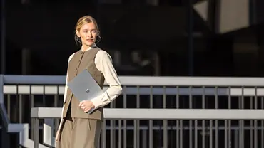 Eine Frau im Business-Look trägt das neue Surface Laptop 7 mit 5G unterm Arm. - Foto: © Microsoft