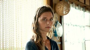 Schauspielerin Svenja Jung steht in einem hellen Raum vor einer Kette aus goldfarbenen Perlen, trägt ein dunkles, locker sitzendes Hemd und blickt ernst, fast nachdenklich, in die Kamera. - Foto: Julia Terjung/Netflix