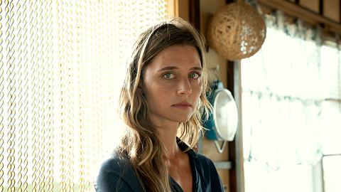 Schauspielerin Svenja Jung steht in einem hellen Raum vor einer Kette aus goldfarbenen Perlen, trägt ein dunkles, locker sitzendes Hemd und blickt ernst, fast nachdenklich, in die Kamera. - Foto: Julia Terjung/Netflix