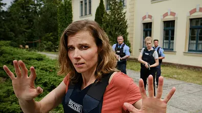 Gorniak steht mit einer Warnweste im Vordergrund des Bildes. Hinter ihr sind drei Polizeipersonen.  - Foto: MDR/W&B Television/Michael Kotschi