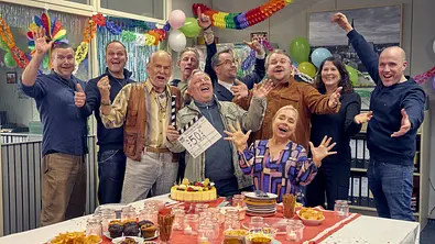 Man sieht den Cast des Münsteraner „Tatort“ an einem feierlich gedeckten Tisch.  - Foto: WDR/Frank Dicks