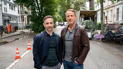 Denis Moschitto und Wotan Wilke Möhring stehen auf einer Hamburger Straße und schauen zufrieden in die Kamera. - Foto: NDR/Georges Pauly Denis Moschitto und Wotan Wilke Möhring stehen auf einer Hamburger Straße und schauen zufrieden in die Kamera. - Foto: NDR/Georges Pauly