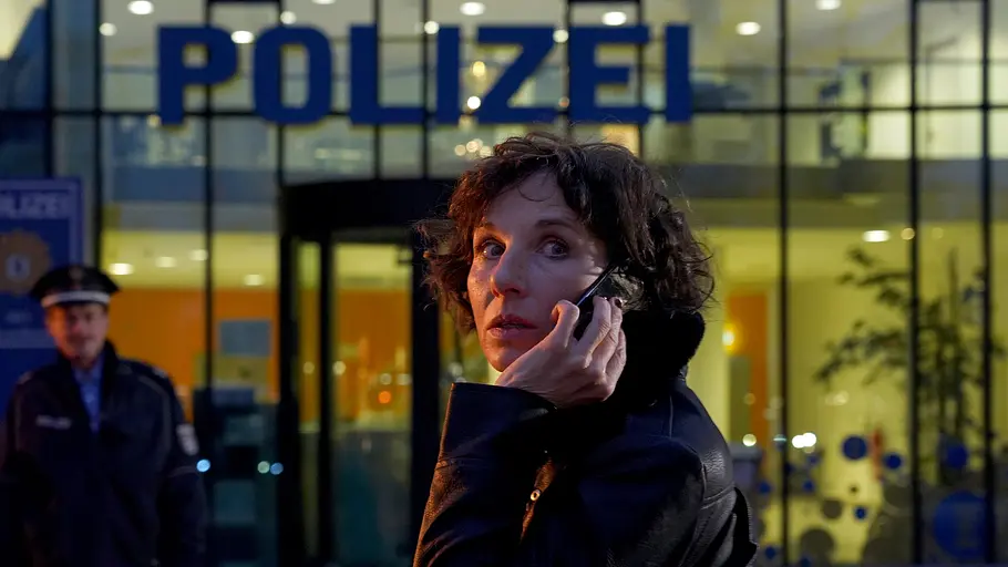 Nina Rubin steht vor der Polizeiwache und telefoniert. 