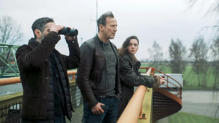 Von links nach rechts: Denis Moschitto hat ein Fernglas in der Hand. Neben ihm stehen Wotan Wilke Möhring und Gaite Jansen.