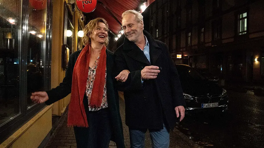 Margarita Broich und Wolfram Koch gehen nachts Arm in Arm eine Straße entlang. 
