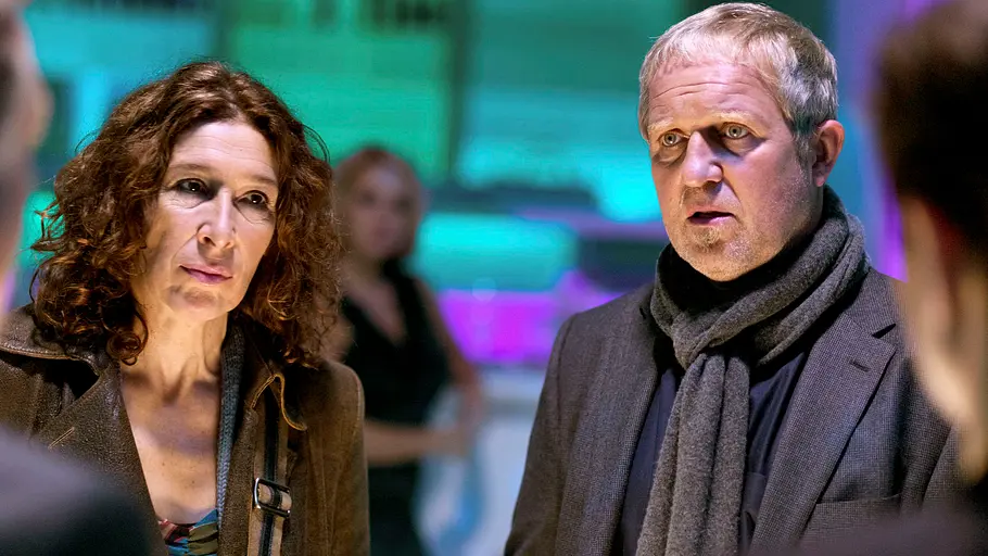 Tatort Adele Neuhauser (l.) und Harald Krassnitzer stehen vor zwei weiteren Personen. Im Hintergrund sind Neonlichter.