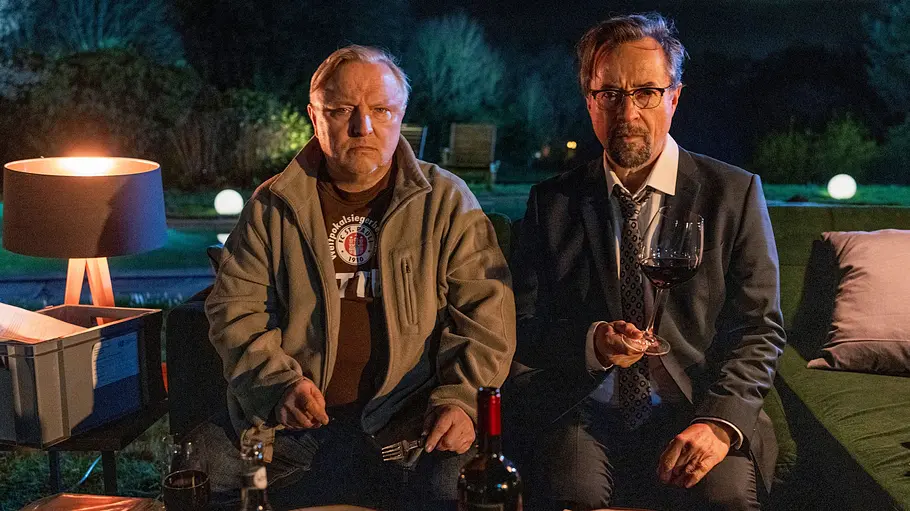 Tatort - Man stirbt nur zweimal Axel Prahl und Jan Josef Liefers sitzen für den Münsteraner „Tatort: Man stirbt nur zweimal“ in einer sommerlichen Lounge und genießen eine Mahlzeit.