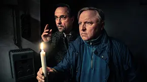 Jan Josef Liefers und Axel Prahl stehen im spärlichen Kerzenschein in der Dunkelheit. - Foto: WDR/Taimas Ahangari Jan Josef Liefers und Axel Prahl stehen im spärlichen Kerzenschein in der Dunkelheit. - Foto: WDR/Taimas Ahangari