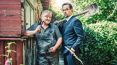 Axel Prahl steht im Blaumann und Jan Josef Liefers im Anzug in einem Schrebergarten. Beide halten Werkzeuge in der Hand. - Foto: WDR/Bavaria Fiction GmbH/Taimas Ahangari Axel Prahl steht im Blaumann und Jan Josef Liefers im Anzug in einem Schrebergarten. Beide halten Werkzeuge in der Hand. - Foto: WDR/Bavaria Fiction GmbH/Taimas Ahangari