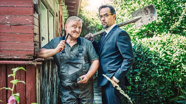 Axel Prahl steht im Blaumann und Jan Josef Liefers im Anzug in einem Schrebergarten. Beide halten Werkzeuge in der Hand. - Foto: WDR/Bavaria Fiction GmbH/Taimas Ahangari Axel Prahl steht im Blaumann und Jan Josef Liefers im Anzug in einem Schrebergarten. Beide halten Werkzeuge in der Hand. - Foto: WDR/Bavaria Fiction GmbH/Taimas Ahangari