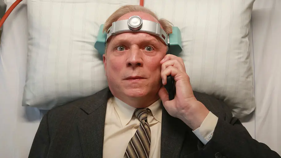 Tatort Murot liegt mit einer Apparatur auf dem Kopf im Bett und telefoniert.
