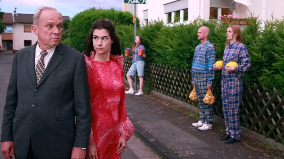 Murot (Ulrich Tukur) steht auf einer ruhigen Straße und wir von mehreren Leuten umgeben.