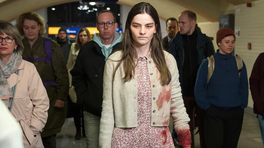 Emilie Neumeister steht in der Mitte des Bildes und schreitet mit blutverschmierten Klamotten durch eine Menschenmenge.