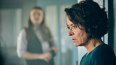 Ulrike Folkerts steht schockiert in der Wache. Hinter steht in der Unschärfe einer ihrer Mitarbeiter. - Foto: SWR/Benoît Linder