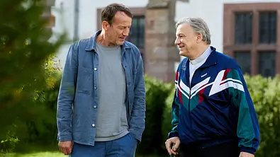 Wotan Wilke Möhring steht für den „Tatort: Schweigen“ neben Hannes Hellmann, der Sportkleidung trägt.  - Foto: ORF/ARD/NDR/Kai Schulz