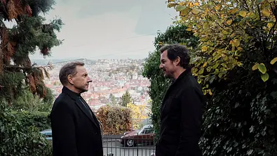 Richy Müller (links) und Felix Klare stehen sich gegenüber und schauen sich an. Hinter ihnen kann man das Stadtbild Stuttgarts erkennen. - Foto: SWR/Benoît Linder