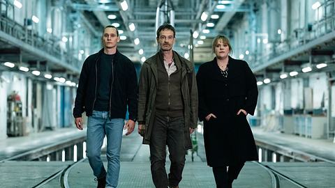Von links nach rechts gehen Rick Okon, Jörg Hartmann und Stefanie Reinsperger durch eine Art Lagerhalle.  - Foto: WDR/Martin Rottenkolber