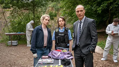 Cornelia Gröschel und Martin Brambach stehen für den Dresdner „Tatort“ an einem See und führen Ermittlungen durch. - Foto:  MDR/MadeFor Film/Steffen Junghans