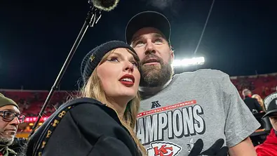 Taylor Swift umarmt Travis Kelce von der Seite. Beide blicken in die Ferne. - Foto: IMAGO / ZUMA Press Wire